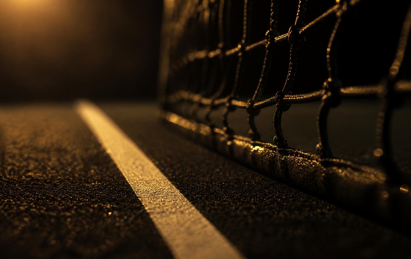 Close-up of a tennis net and court line lit by warm floodlight at night